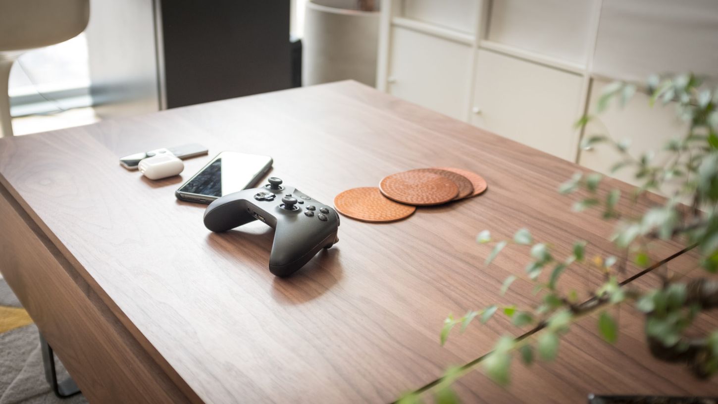 Gaming controller, smartphone, and earbuds arranged on a walnut coffee table. Modern tech lifestyle photography.